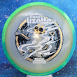 Load image into Gallery viewer, Top-down view of an Axiom Aspect fairway driver disc golf disc in Eclipse Glow plastic with a lime green and blue overmold rim and a black, white, and gold holographic foil Simon Lizotte Halloween Tour Series stamp.
