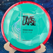 Load image into Gallery viewer, Top-down view of a teal Axiom Time Lapse distance driver disc golf disc with a red swirl rim in Neutron plastic featuring a silver holo and black foil Simon Line stamp.
