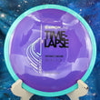 Load image into Gallery viewer, Top-down view of a purple Axiom Time Lapse distance driver disc golf disc with a teal swirl rim in Neutron plastic featuring a silver holo and black foil Simon Line stamp.
