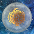 Load image into Gallery viewer, Top-down view of a brand-new white and clear sparkle DGA Aftershock midrange disc golf disc in SP Line plastic with a gold foil Gravity Black Hole custom stamp.
