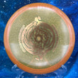 Load image into Gallery viewer, Top-down view of an orange sparkle DGA Rift midrange disc golf disc in SP Line plastic featuring a gold foil Black Hole special edition stamp.
