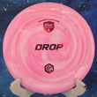 Load image into Gallery viewer, Top-down view of a pink and white swirled Discmania Drop approach disc golf disc in Swirl S-Line plastic with a red holographic foil Niklas Anttila Creator Series stamp.

