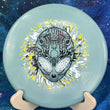 Load image into Gallery viewer, Top-down view of a light teal Infinite Discs Cohort putt and approach disc golf disc in I-Blend plastic with a black, white, and yellow three-foil Neon Alien Head stamp.
