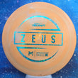 Load image into Gallery viewer, Top-down view of an orange pre-owned Discraft Zeus distance driver disc golf disc featuring a Paul McBeth foil stamp rated 8/10 condition.
