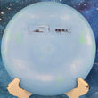 Load image into Gallery viewer, Top-down view of a light blue Innova Destroyer in Star plastic. The disc features a rectangular black "F2 Factory Second" stamp in the center and is displayed on a white stand against a starry background.
