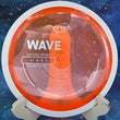 Load image into Gallery viewer, Top view of a Neon Orange Proton MVP Wave distance driver featuring the Project Lab Coat white GYRO rim and a silver tri-foil stock stamp, 173g, 10/10 condition.
