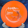 Load image into Gallery viewer, Pre-owned orange Innova Gator Glow Champion plastic midrange disc, 175g, featuring a silver foil Gator and basket stamp with "Patient #" text in uninked 8.5/10 condition.
